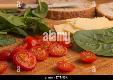 Tomates cerise parmi d'autres ingrédients. Faire un sandwich sur une planche en chêne. Banque D'Images