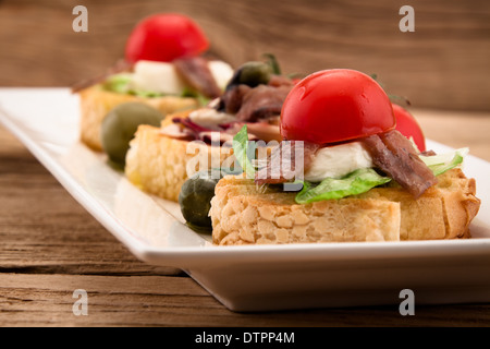 Crostini avec anchois mozzarella et tomate sur planche de bois Banque D'Images