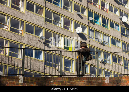 Un jeune homme est debout sur un rail métallique dans un bloc d'appartements abandonnés. Il y a des fenêtre cassée de verres et les antennes paraboliques. Banque D'Images