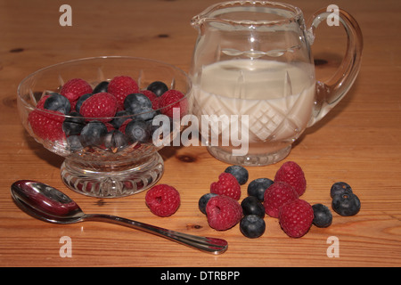 Les framboises et les bleuets dans un cristal de verre sundae et la crème dans un pot sur une table en pin avec une cuillère (2 sur 11) Banque D'Images