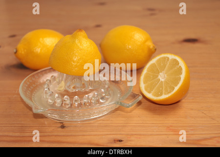 Un demi citron soit écrasé sur un presse-agrumes en verre/centrifugeuse avec deux citrons et demi en arrière-plan sur pin (3 de série de 4) Banque D'Images