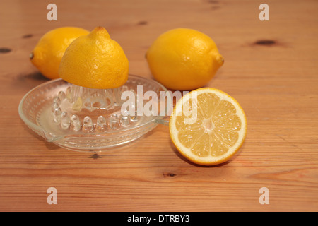 Un demi citron soit écrasé sur un presse-agrumes en verre/centrifugeuse avec deux citrons et demi en arrière-plan sur pin (4 de série de 4) Banque D'Images