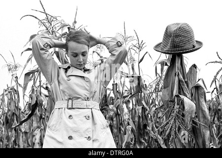 Modèle de mode des années 60 avec l'imperméable de poser dans un champ de maïs Banque D'Images