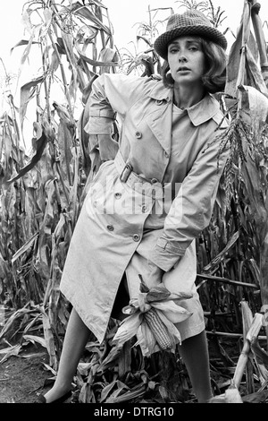 Modèle de mode des années 60 avec l'imperméable et le chapeau de poser dans un champ de maïs Banque D'Images