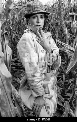 Modèle de mode des années 60 avec l'imperméable et le chapeau de poser dans un champ de maïs Banque D'Images