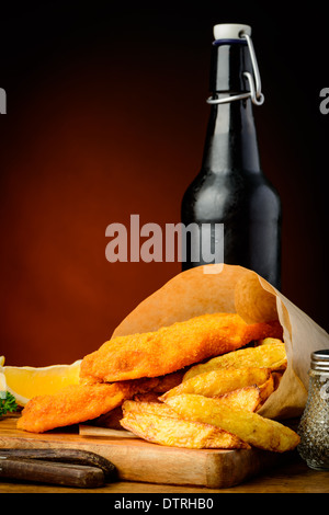 Fish and chips traditionnel enveloppé dans du papier et bouteille de bière Banque D'Images