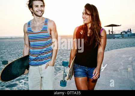 Couple carrying skateboards on beach Banque D'Images
