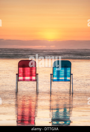 Les chaises de parterre en vagues sur la plage au coucher du soleil Banque D'Images