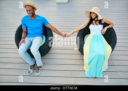 Couple holding hands in chaises en osier Banque D'Images