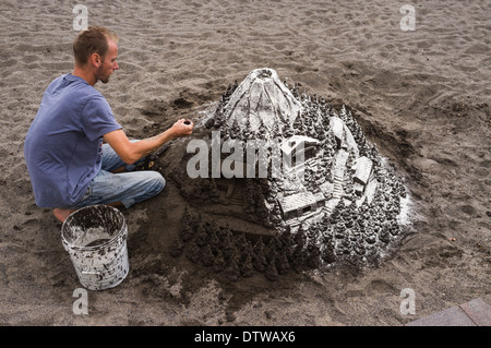 Sculpteur de sable au travail faire une montagne couverte de neige scène à la plage d'El Medano, Tenerife, Canaries, Espagne Banque D'Images