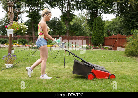 Coupe femme le jardin fleuri avec une tondeuse électrique Banque D'Images