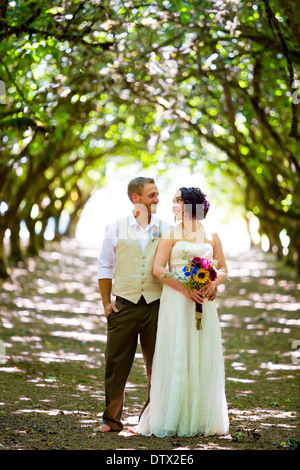 Mariée et le marié de poser pour un portrait dans un verger en contre-jour le jour de leur mariage dans l'Oregon avec lumière filtrant à travers les arbres. Banque D'Images