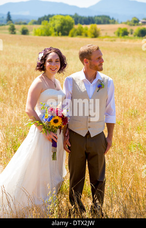 Jeunes mariés ensemble le jour de leur mariage à travers un champ dans l'Oregon. Banque D'Images