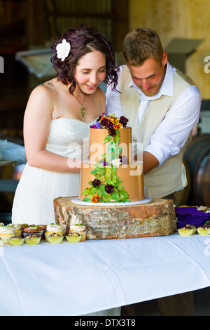 Mariée et le marié couper leur gâteau de mariage lors d'une réception avec un thème de l'arbre. Banque D'Images