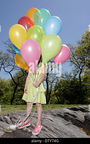 Mixed Race girl réalisation colorful balloons in park Banque D'Images