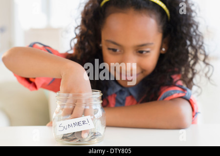 Mixed Race girl putting coins in summer savings jar Banque D'Images