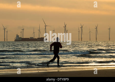 Jogger sur Seaton Carew plage près de Hartlepool au lever du soleil. Parc éolien offshore de Teesside en distance. L'Angleterre. UK Banque D'Images