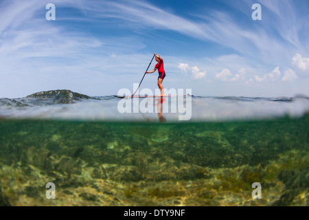 Une fille dans un rash vest paddleboards rouge dans les eaux claires du North Devon UK SUP (stand up paddleboarding) Banque D'Images