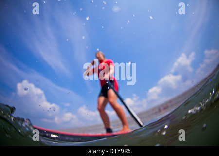 Une fille dans un rash vest paddleboards rouge dans les eaux claires du North Devon UK SUP (stand up paddleboarding) Banque D'Images