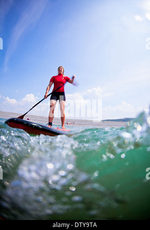 Une fille dans un rash vest paddleboards rouge dans les eaux claires du North Devon UK SUP (stand up paddleboarding) Banque D'Images