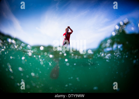 Une fille dans un rash vest paddleboards rouge dans les eaux claires du North Devon UK SUP (stand up paddleboarding) Banque D'Images