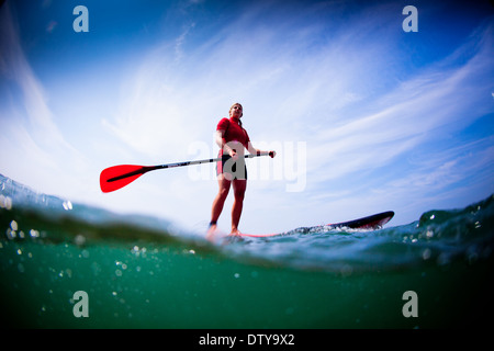 Une fille dans un rash vest paddleboards rouge dans les eaux claires du North Devon UK SUP (stand up paddleboarding) Banque D'Images