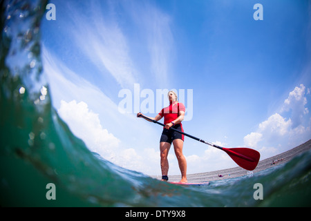 Une fille dans un rash vest paddleboards rouge dans les eaux claires du North Devon UK SUP (stand up paddleboarding) Banque D'Images