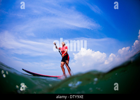 Une fille dans un rash vest paddleboards rouge dans les eaux claires du North Devon UK SUP (stand up paddleboarding) Banque D'Images
