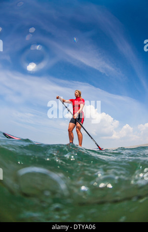 Une fille dans un rash vest paddleboards rouge dans les eaux claires du North Devon UK SUP (stand up paddleboarding) Banque D'Images