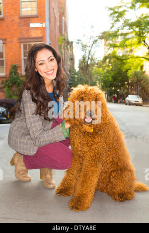 Mixed Race woman petting dog on city street Banque D'Images