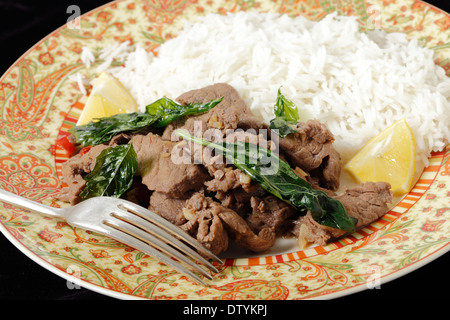 Boeuf au Chili avec feuilles de basilic frit croustillant, servi avec riz basmati blanc et des quartiers de citron. Banque D'Images