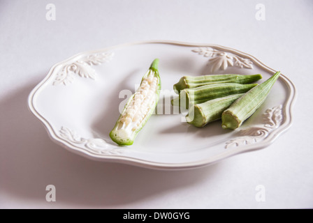 Gombo frais gousses non cuits sur un plat blanc, avec une coupe montrant les graines. Banque D'Images