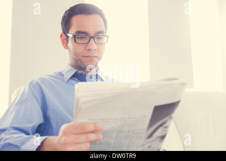 Unsmiling man reading a newspaper Banque D'Images