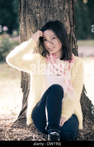 Femme assise contre un arbre Banque D'Images