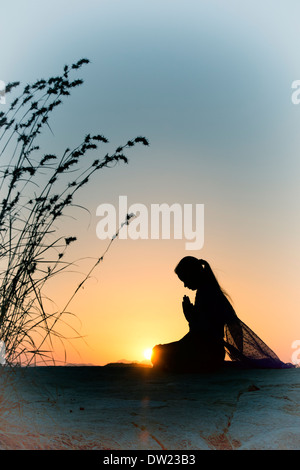 Indian woman praying au coucher du soleil dans la campagne indienne. Silhouette. Appliqué avec filtre nostalgique Banque D'Images