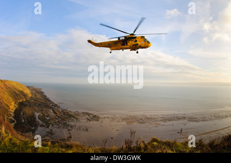 Un hélicoptère de sauvetage de la RAF jaune avec deux membres de l'équipe debout dans la porte ouverte qu'elle vole au-dessus de la baie de St Francis Bay, North Yorkshire. Banque D'Images