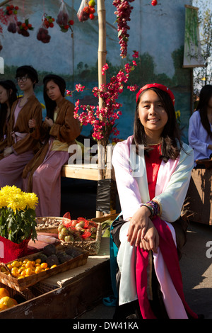 Une jeune vietnamienne en costume traditionnel se trouve à côté d'un petit bateau servant à vendre des fruits et des légumes à un festival de Tet Banque D'Images