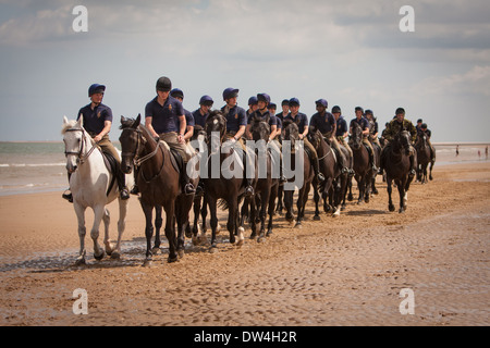 Cavaliers et les femmes du blues et de la famille royale l'exercice de leurs chevaux dans le surf à Holkham Beach Norfolk, Royaume-Uni Banque D'Images