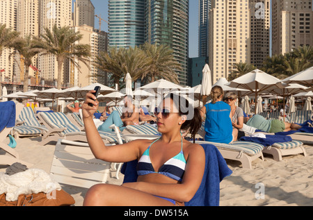 Jeune femme âgée de 20 ans de prendre une photo selfies sur la plage, la plage de Jumeirah, Dubai, Émirats arabes unis, Moyen Orient ÉMIRATS ARABES UNIS Banque D'Images