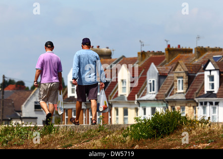 Deux hommes transportant des magasins le long de la rue housing estate, St Leonards on Sea, East Sussex, Angleterre Banque D'Images