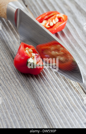 Deux moitiés d'un piment Habanero couché avec un couteau de cuisine, sur une table en bois rustique Banque D'Images