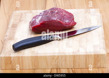 Pièce de filet de boeuf cru se trouve sur une planche à découper avec un couteau de cuisine Banque D'Images