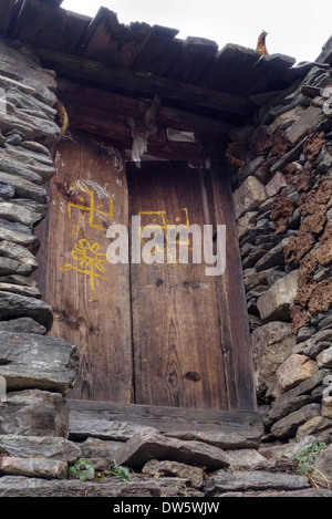 Symboles peints, y compris les croix gammées, sur la porte d'une maison tibétaine dans la vallée de la Tsum du Népal. Banque D'Images