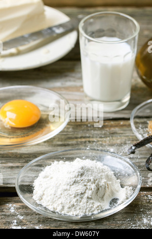 Soucoupe de farine, d'œuf et verre de lait sur la vieille table en bois. Banque D'Images