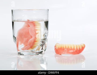 Un ensemble de dentier dans un verre d'eau sur un fond blanc Banque D'Images