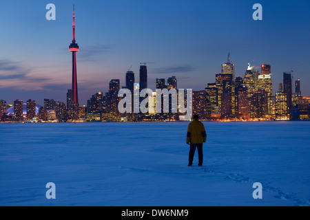 Homme marchant dans la neige au crépuscule sur le lac Ontario avec des lumières de Toronto city skyline en hiver Banque D'Images