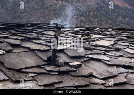 La fumée de bois sortant d'une cheminée sur une maison avec une toiture en ardoise dans la région du Manaslu au Népal. Banque D'Images