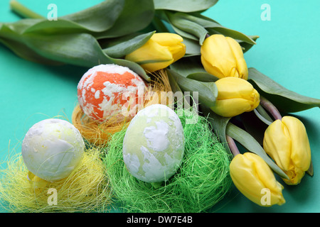 Les oeufs de Pâques dans les supports et mouchetée tulipes jaunes sur fond vert Banque D'Images