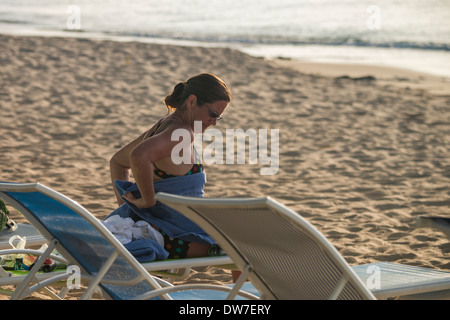 Une femme de race blanche dans la trentaine se détend sur une chaise de plage et sèche au bout de quelques brasses, près du bord de la mer des Caraïbes. Banque D'Images