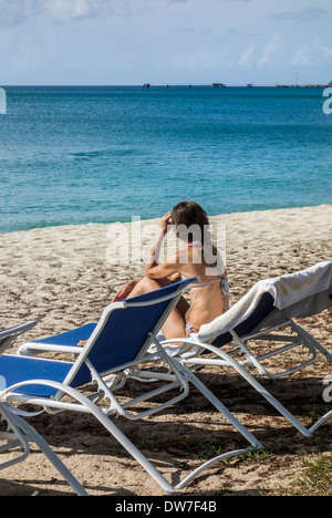 Une femme de race blanche d'une quarantaine d'années, se détend sur une chaise de plage sur la plage de sable et donne sur la mer des Caraïbes, à Sainte-Croix. Concept Banque D'Images